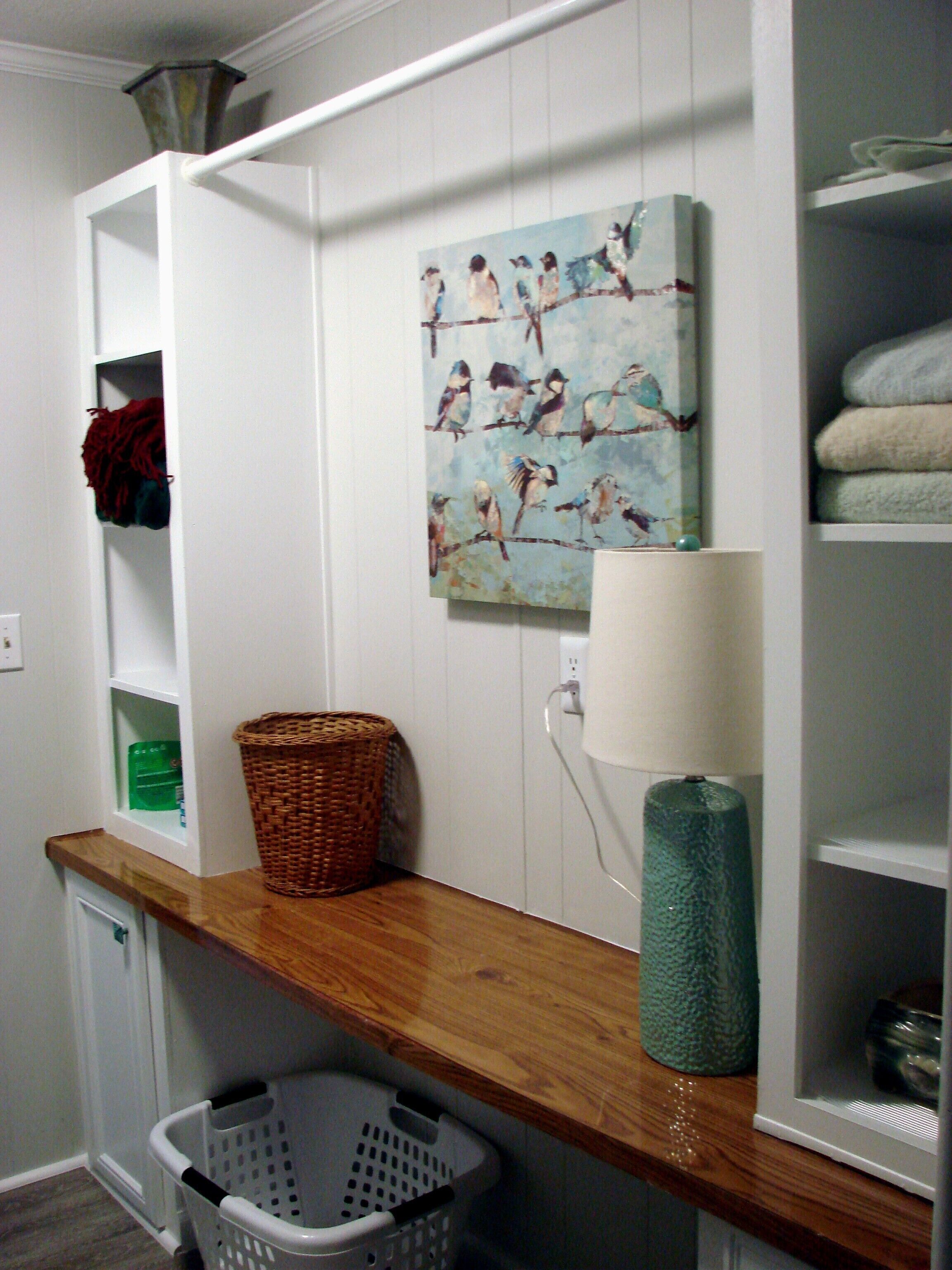 A laundry area with a wooden shelf, a basket, a washing machine, and a wall-mounted lamp.