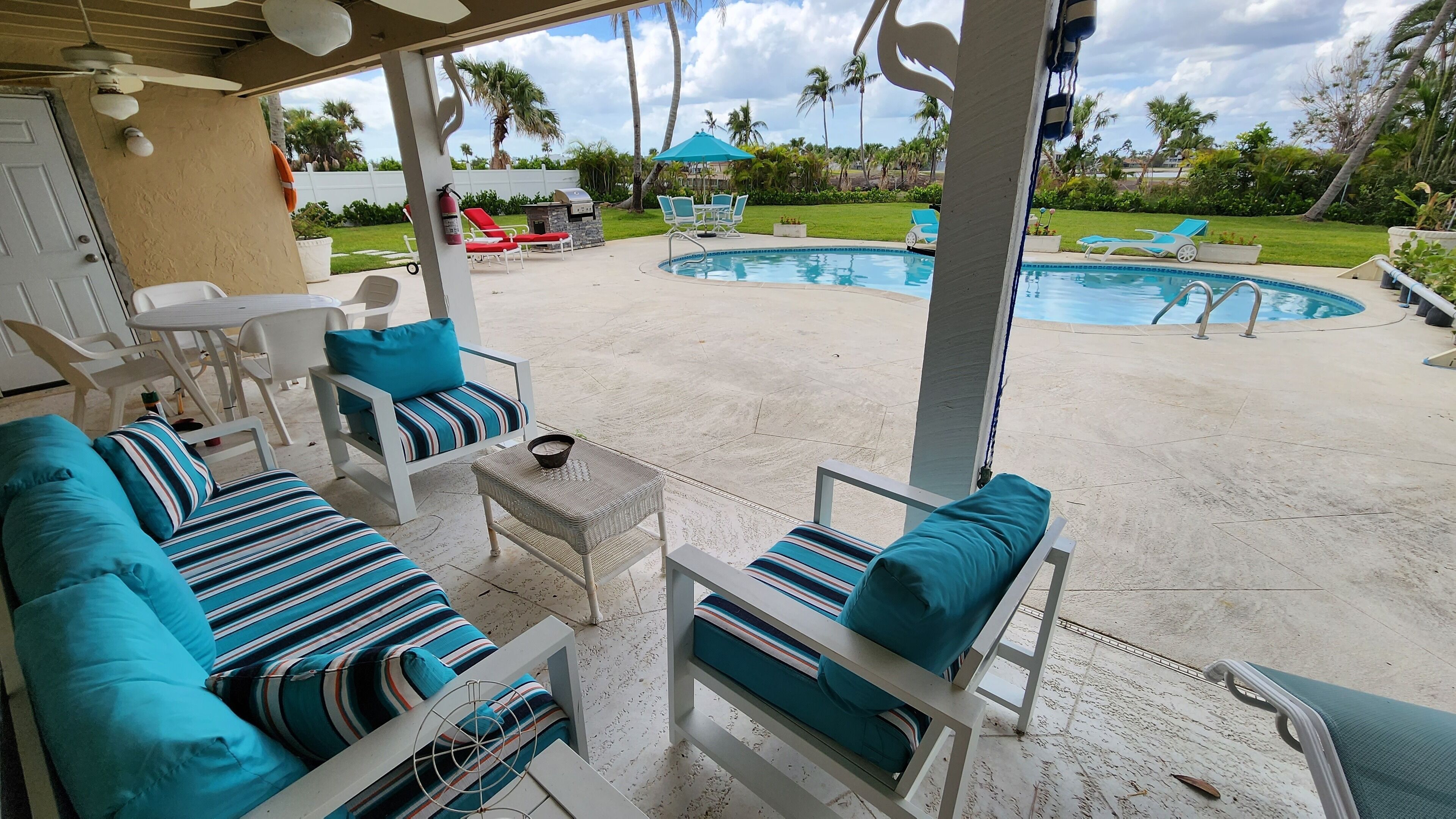 A covered outdoor seating area with a pool and lounge chairs.