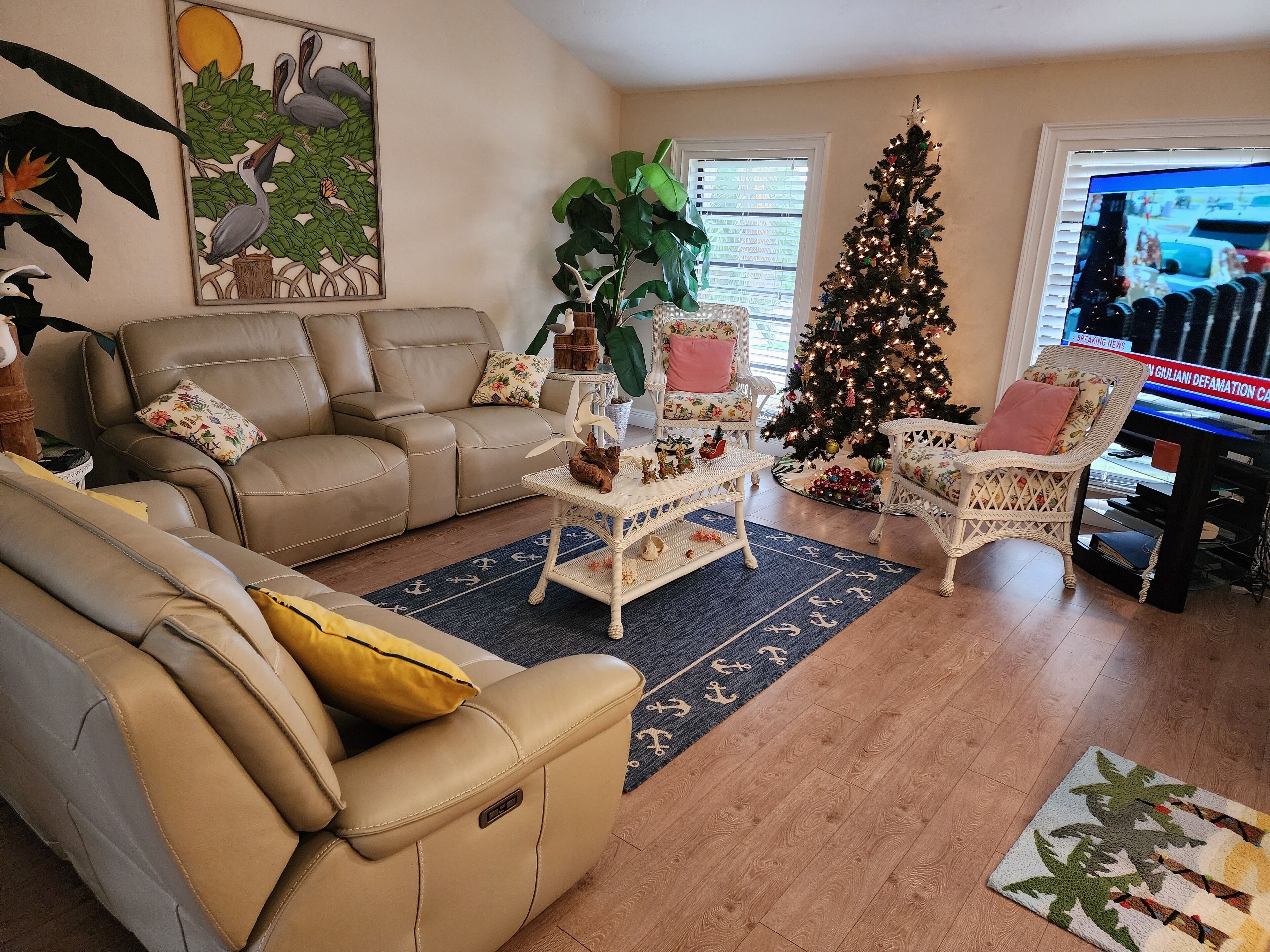 A living room with a beige sofa, a white coffee table with decorative items, a Christmas tree, and a television.