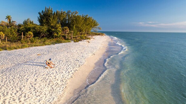 A beach with clear turquoise water, white sand, and dense green vegetation along the shoreline. - SANIBEL SUN CASTLE  Splendid home, heated pool, great location, bike to beach. (Sanibel)