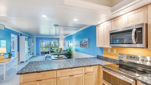 A modern kitchen with wooden cabinets, granite countertops, stainless steel appliances, and a dining area with a table and chairs. - Rare Walkout Condo On Sanibel Beach (Sanibel)