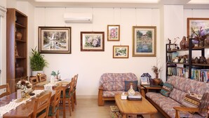 A cozy living room with a wooden dining table, chairs, a sofa, and a bookshelf filled with books and decorative items. - Pottery Flower B&B (Jiji)