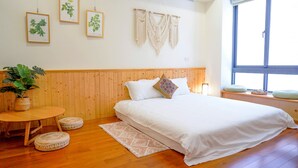 A bedroom with a wooden headboard, a bed with white bedding, a round wooden table with a plant, and a window with a view. - Pottery Flower B&B (Jiji)