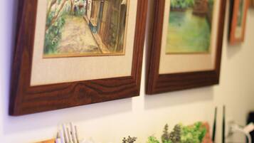 Framed artwork on a wall, a wooden shelf with potted plants, and a framed picture leaning against the shelf.