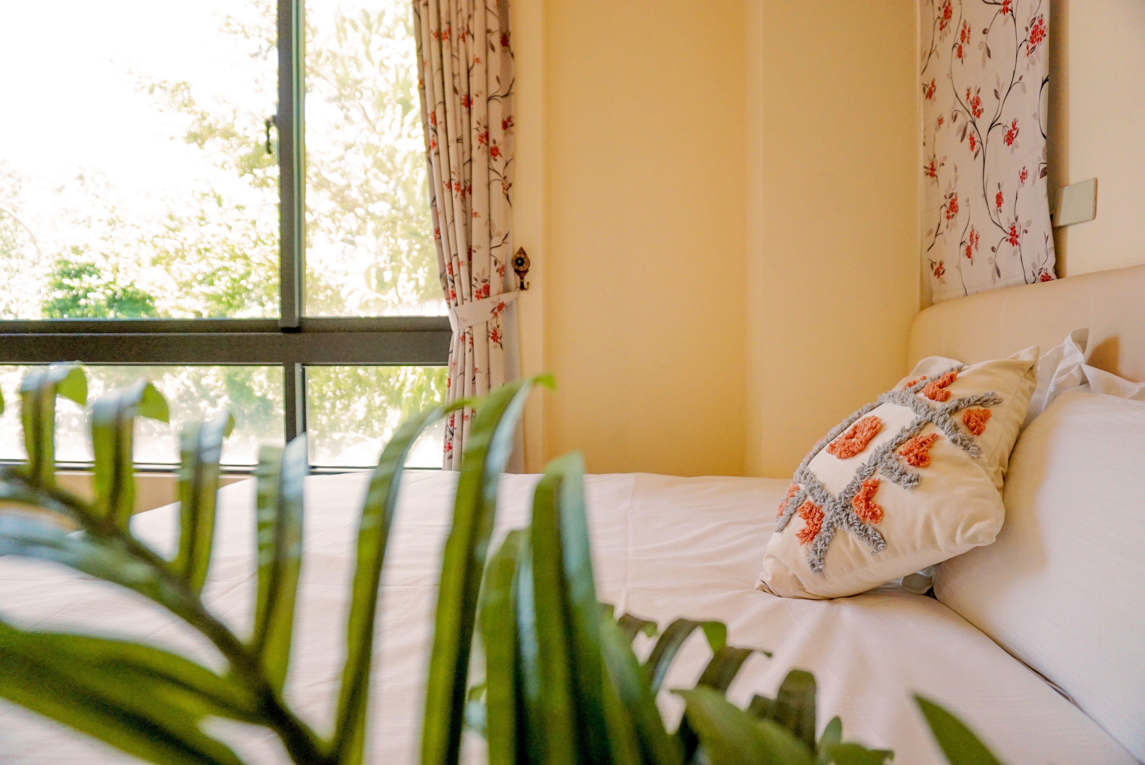 Quarto com cama, cortinas florais e janela com vista para árvores.