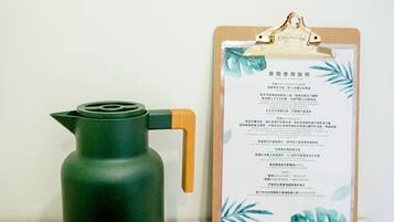 A room with a wooden table, a green kettle, and a clipboard with a menu.
