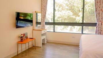 A bedroom with a bed, a desk, a TV mounted on the wall, and a window with curtains.