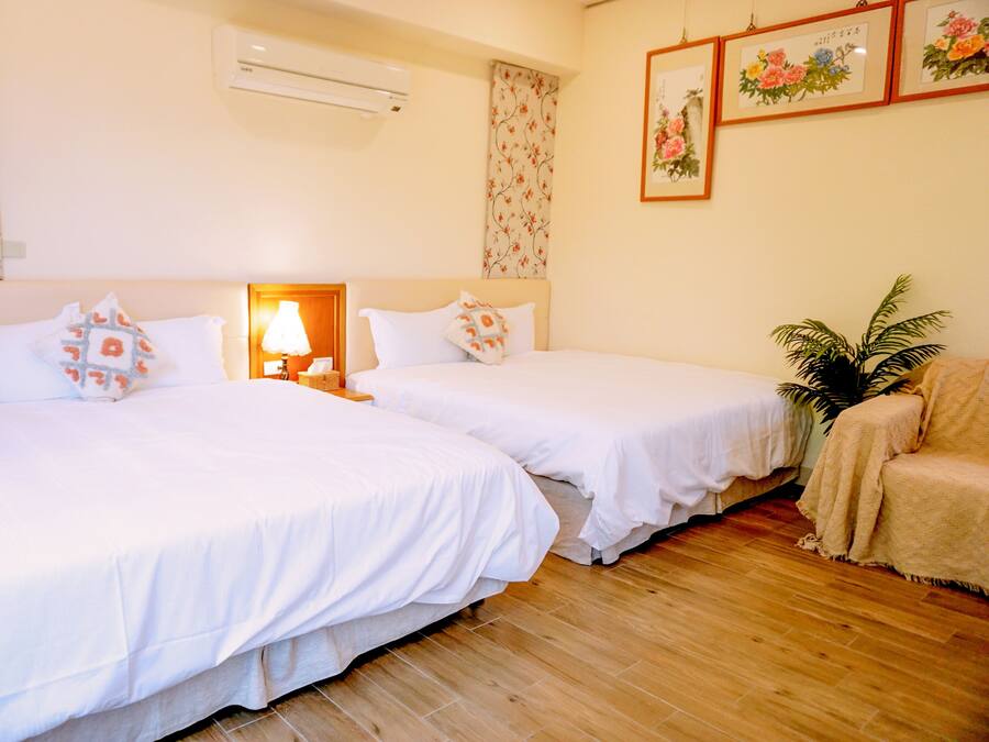 Habitación de hotel con dos camas, una mesita de noche con lámpara, papel tapiz floral y cuadros en la pared.
