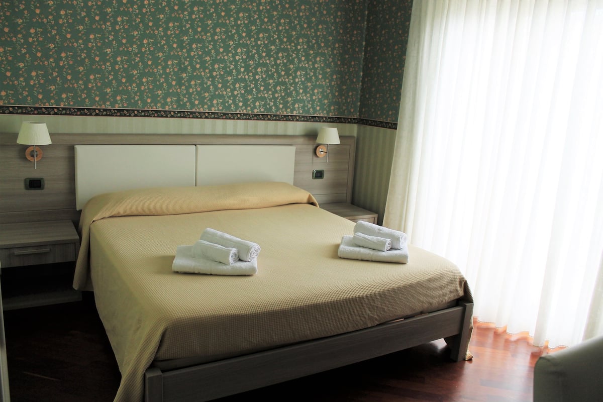 Una cama bien tendida con dos toallas, una mesita de noche con lámpara y un estampado floral en el papel tapiz.