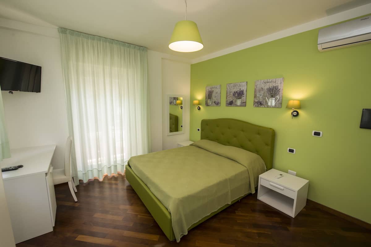 Un dormitorio con cama, escritorio, silla, mesita de noche y televisor instalado en la pared.