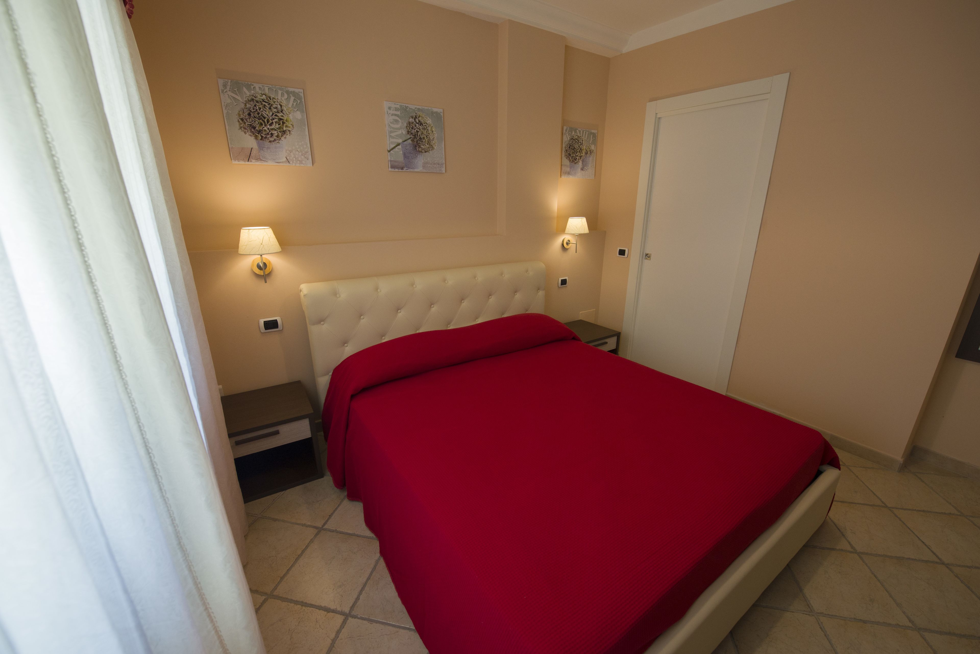 Ein Schlafzimmer mit einer gepolsterten Kopfteile, einer roten Bettdecke, zwei Wandleuchten und zwei an der Wand befestigten Kunstwerken.