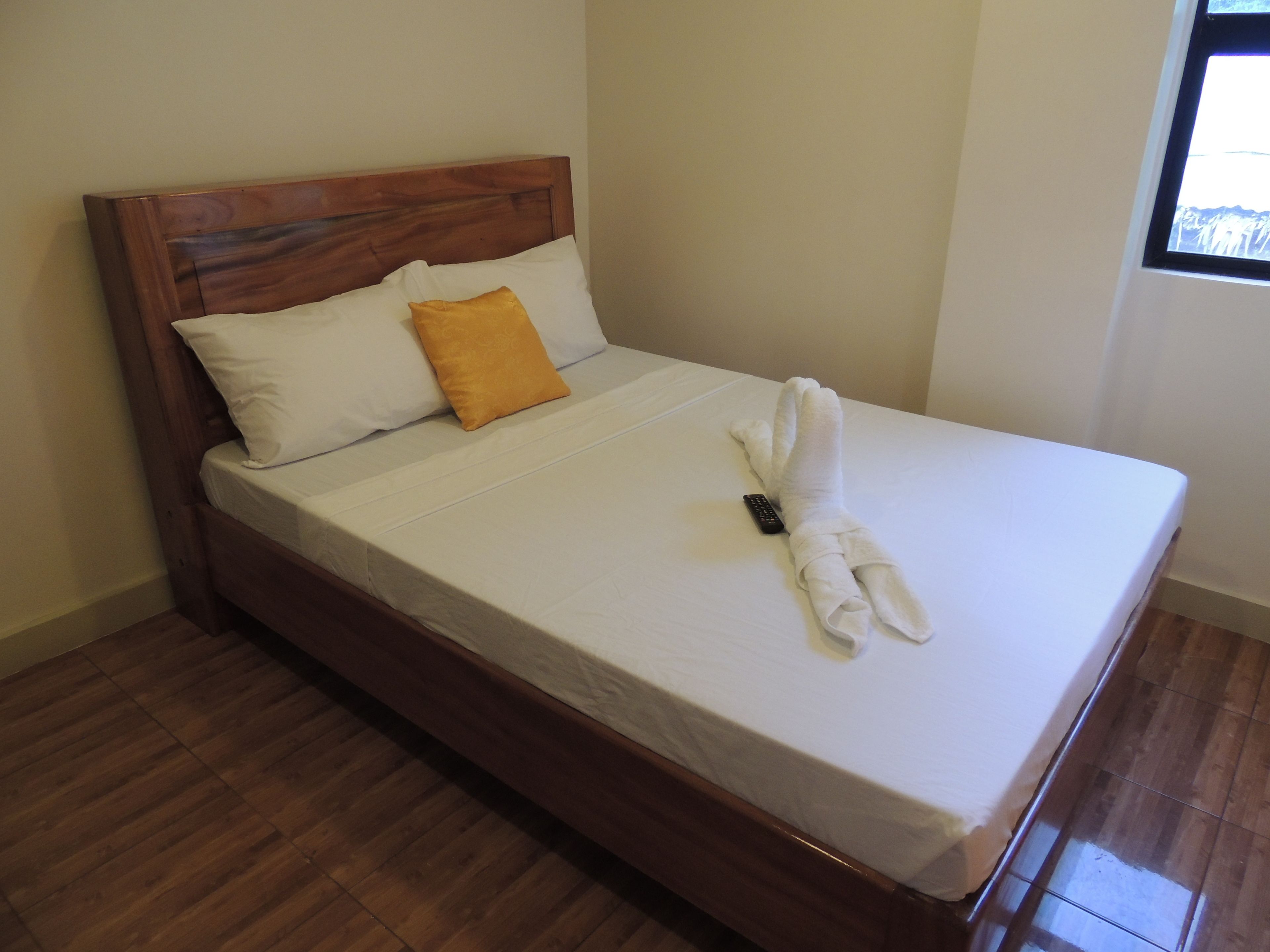 A neatly made bed with white sheets, a wooden headboard, a single yellow pillow, and a towel folded on the bed.