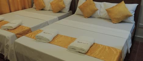 Two twin beds with white linens and gold accents, each with a folded towel and a pillow.