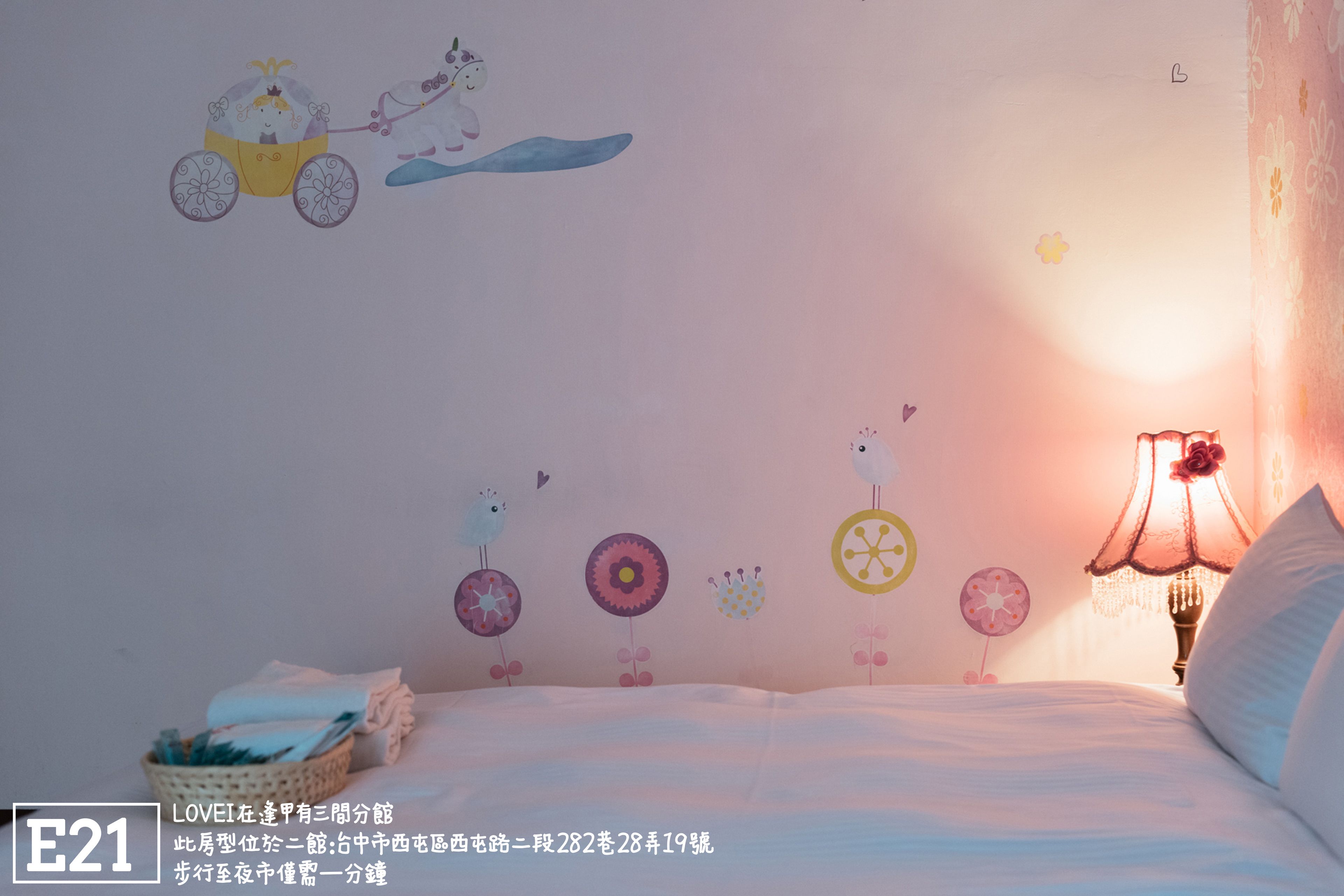 A bedroom with a bed, a nightstand, a lamp, and a wall decorated with children's drawings.