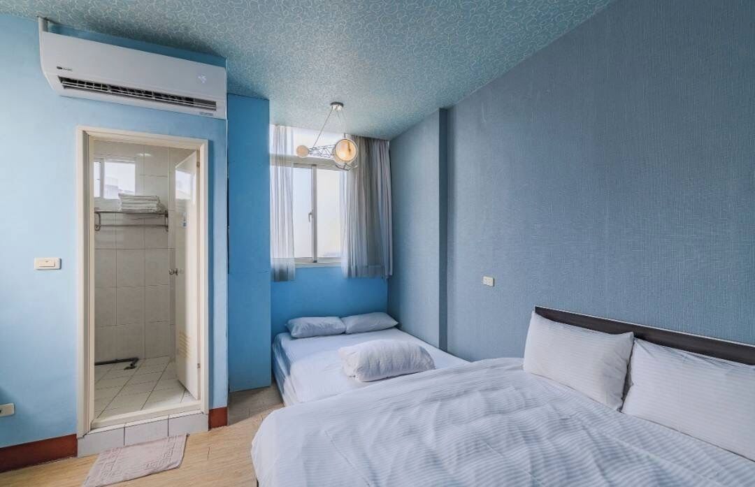 A bedroom with two beds, a shower, and a window with curtains.