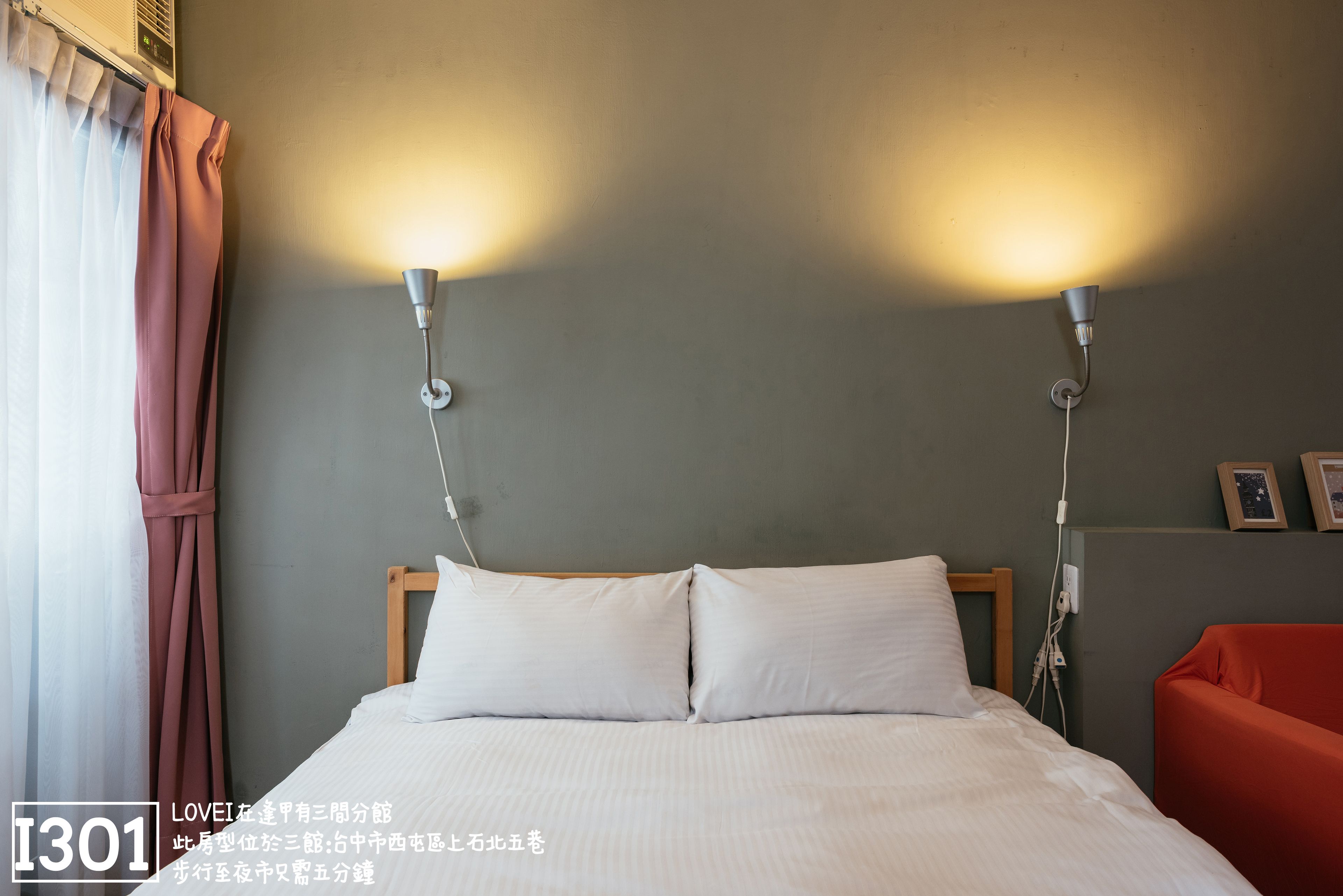 A hotel room with a bed, two wall-mounted lamps, a red chair, and a curtain.