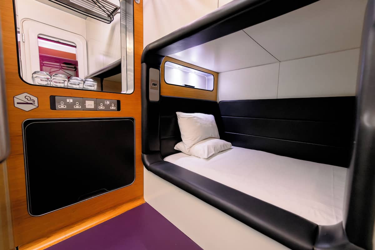 A compact train cabin with a single bed, a small window, and a mirror.