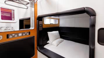 A compact, modern train cabin with a single bed, a small table with a mirror, and a window with a view of the outside.