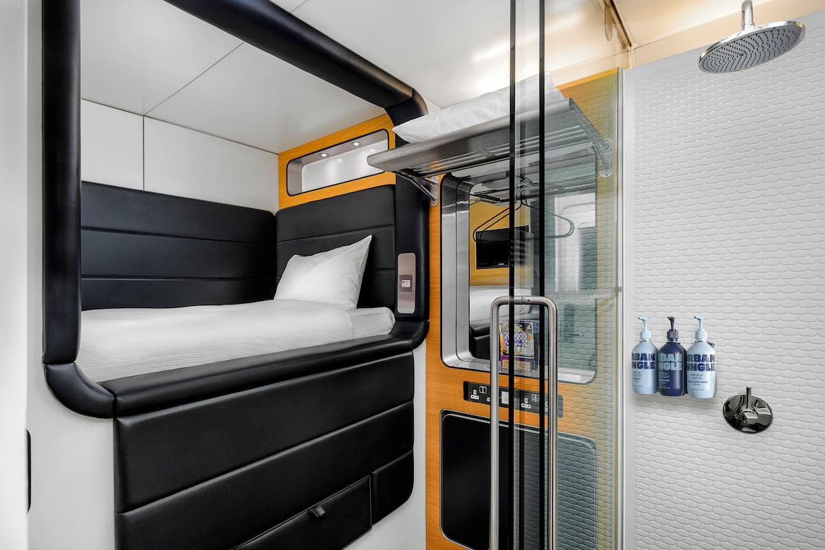 A compact, modern bathroom with a shower, a small bed, and toiletries.