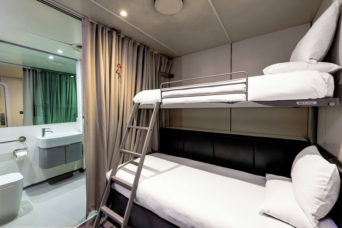 A bunk bed with a ladder, a sink, and a mirror in a modern room.