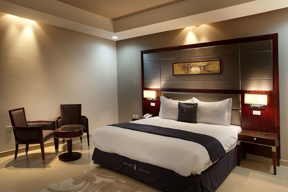 A modern hotel room with a large bed, two bedside tables, a desk, and two chairs.