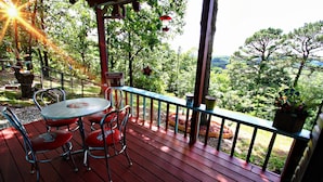 Terraza de madera con mesa y sillas, rodeada por una barandilla y vistas a un paisaje exuberante.