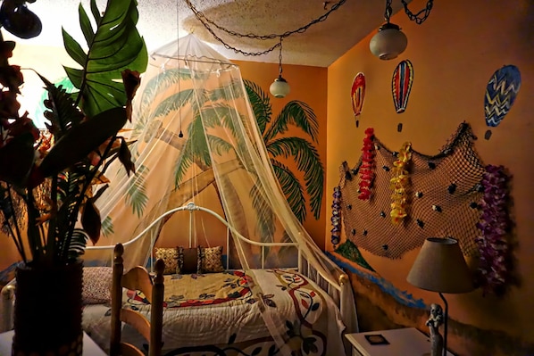 Une chambre avec un lit sous un dais, un mur décoré de peintures murales représentant des palmiers et un élément décoratif suspendu au mur.