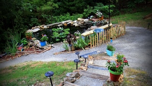 Un jardín con un estanque, terraza de madera y plantas en macetas.