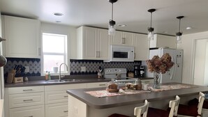 A modern kitchen with white cabinets, a central island with seating, a microwave, and a refrigerator.