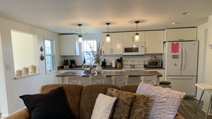 A modern kitchen with white cabinets, a central island, and a dining area with a brown couch.