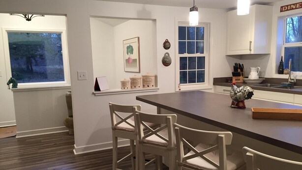 A modern kitchen with a central island, bar stools, a window with a view, and a 'DINE' sign on the wall.