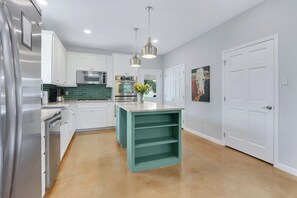 A modern kitchen with white cabinets, stainless steel appliances, and a teal island. - Artista I 2/2 with New Pool, Hot tub,  Pool Table (Wimberley)