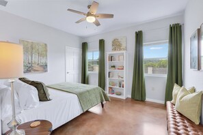 A bedroom with a bed, a nightstand, a lamp, a bookshelf, and a view of the outdoors. - Artista I 2/2 with New Pool, Hot tub,  Pool Table (Wimberley)
