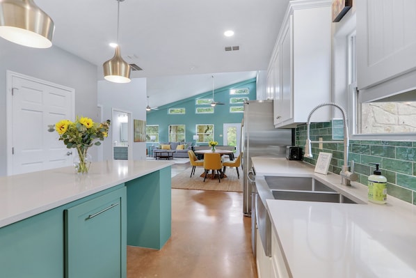 A modern kitchen with teal cabinetry, a central island, and a dining area with yellow chairs.