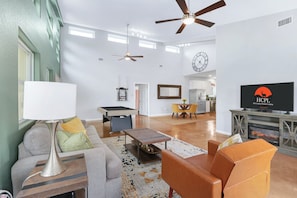 A modern living room with a pool table, sofas, a TV, and ceiling fans.