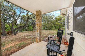 A covered porch with a stone pillar, a bench, and a view of a wooded area.