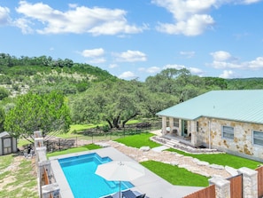 A backyard with a swimming pool, a stone house, and a green lawn.