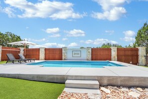 A swimming pool with a stone wall and the word "ARTISTA" on it, surrounded by a wooden fence and a white umbrella.