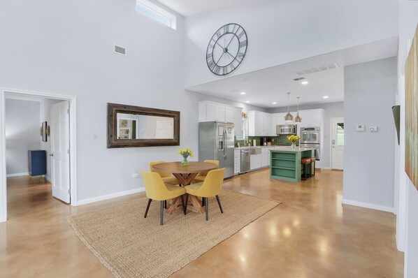 A spacious kitchen with modern appliances, a dining area with yellow chairs, and a large wall clock.