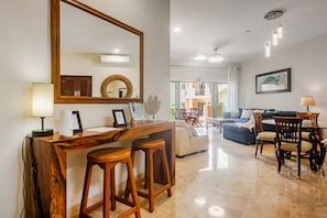 A spacious living area with a wooden bar, two stools, a sofa, and a dining table with chairs.