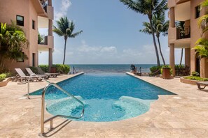 A swimming pool with a view of the ocean, surrounded by palm trees and lounge chairs.