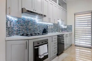 A modern kitchen with a gas stove, oven, and dishwasher, featuring a tiled backsplash and white cabinetry.