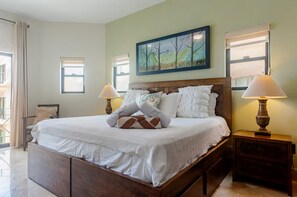 A hotel room with a large bed, two bedside lamps, a painting above the bed, and a window with curtains.