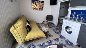 A compact living space with a sofa, a small table with a basket, a washing machine, and a TV mounted on the wall.