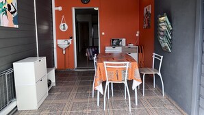 A compact room with a dining table, chairs, a small refrigerator, a sink, a clock, and a wall-mounted TV.