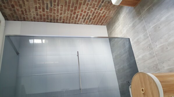 Un baño moderno con cabina de ducha de vidrio, tocador de madera y pared de ladrillo.