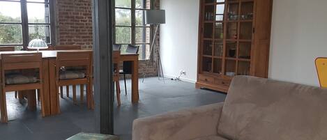 A spacious living area with a wooden dining table, chairs, a beige sofa, and a large wooden cabinet.