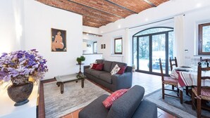 Ein modernes Wohnzimmer mit grauem Sofa, einem Couchtisch und einem Topf mit Pflanze. Es gibt einen Essbereich mit Tisch und Stühlen.