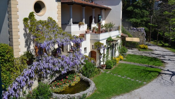 Ein zweigeschossiges Haus mit Balkon, rundem Fenster und einem Garten mit violetten Blumen.