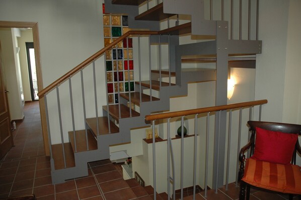 A multi-level staircase with wooden handrails and metal railings, leading to a landing with a chair and a red cushion.